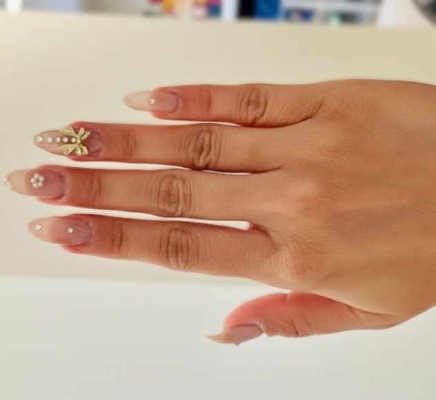 Sheer nude nails finished with a gold bow and tiny pearl details