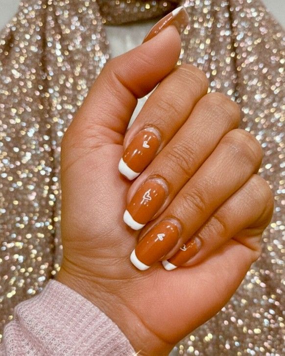 Warm caramel nails with a crisp white French tip and hand-painted white hearts