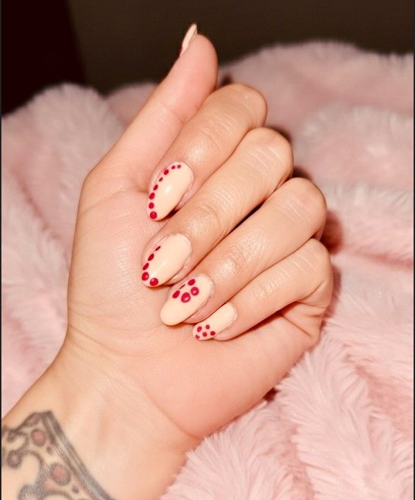 Soft nude almond nails decorated with small deep red dots